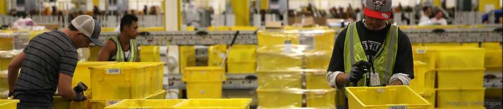 Two employee sorting yellow plastic boxes in Amazon fulfillment center.
