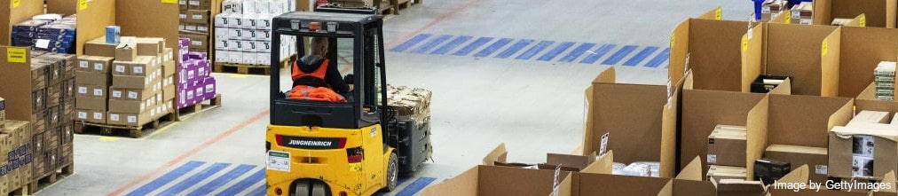 An employee in Amazon fulfillment center moving a pallet of boxes using a forklift