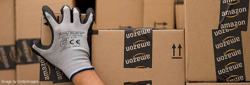 Amazon employee in gray glove picking up a box with Amazon logo stickers