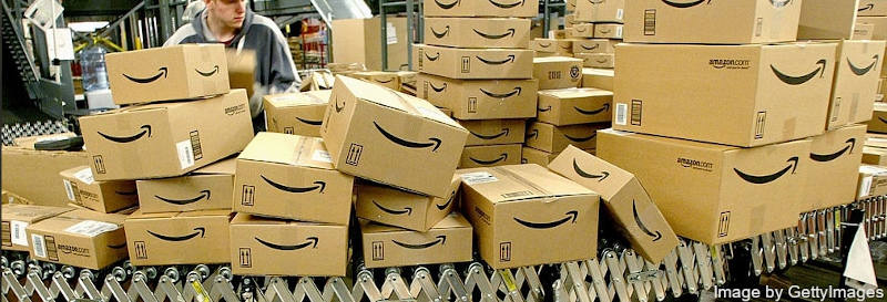 Amazon employee watching at conveyor belt full of boxes with Amazon.com logos