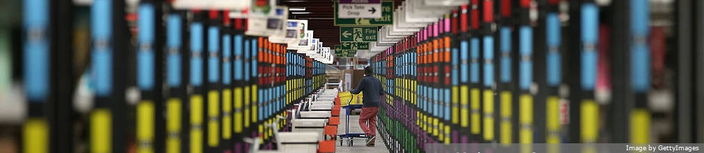 Amazon employee with a trolly is standing between high shelves and sorting packages.