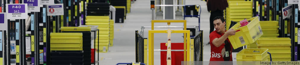 Amazon employee loads yellow plastic boxes on a conveyor of FBA center