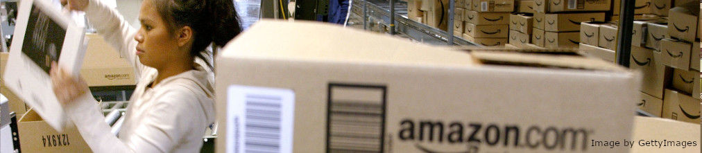 Amazon fulfillment center employee surrounded by carton boxes with Amazon logo is sorting products