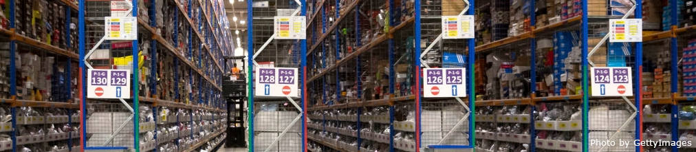 An employee in Amazon fulfillment center moving boxes from a higher shelf using a forklift