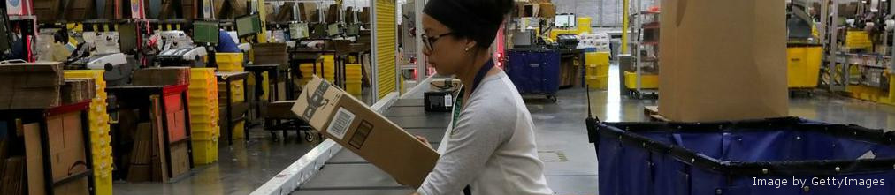 Amazon employee looking at carton box on the transporter tape of the fulfilment center