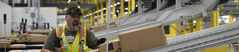An employee in a yellow vest took a cardboard box from conveyor tape at the Amazon fulfillment center