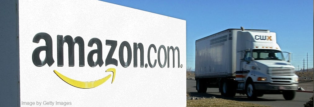 A truck passing Amazon fulfillment center with Amazon.com logo on billboard