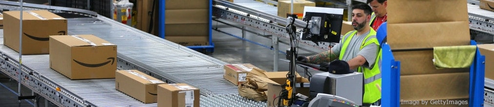 Amazon employee in yellow vest watching in monitor and operates conveyor belt in Amazon fulfillment center